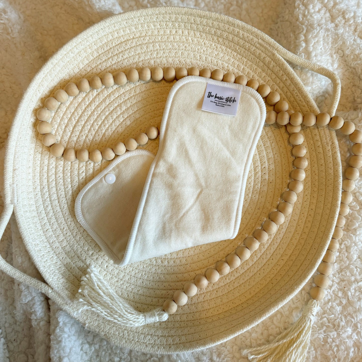 4 Layer hemp cotton booster featured on a woven rope basket with a decorative wooden ball garland