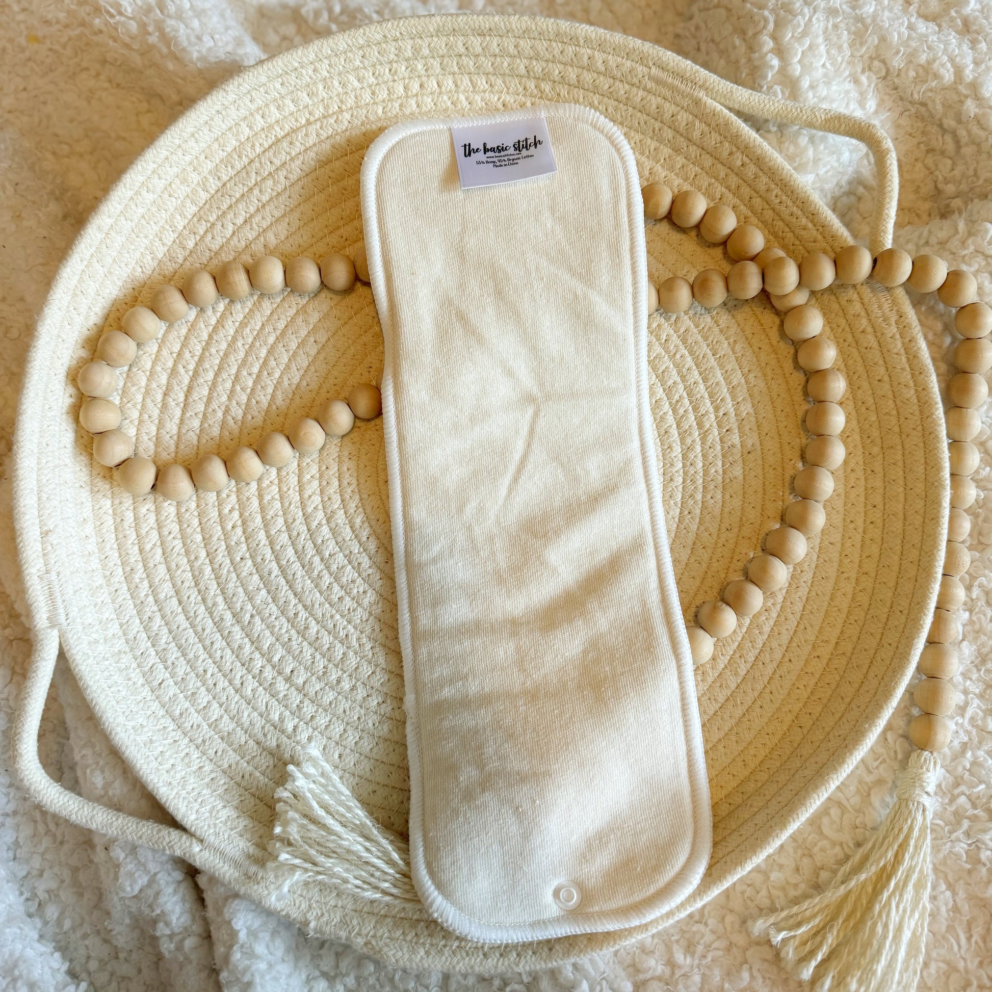 4 Layer hemp cotton booster featured on a woven rope basket with a decorative wooden ball garland